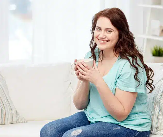 A happy woman holding a cup of coffee, symbolizing a positive and relaxed approach to weight loss.